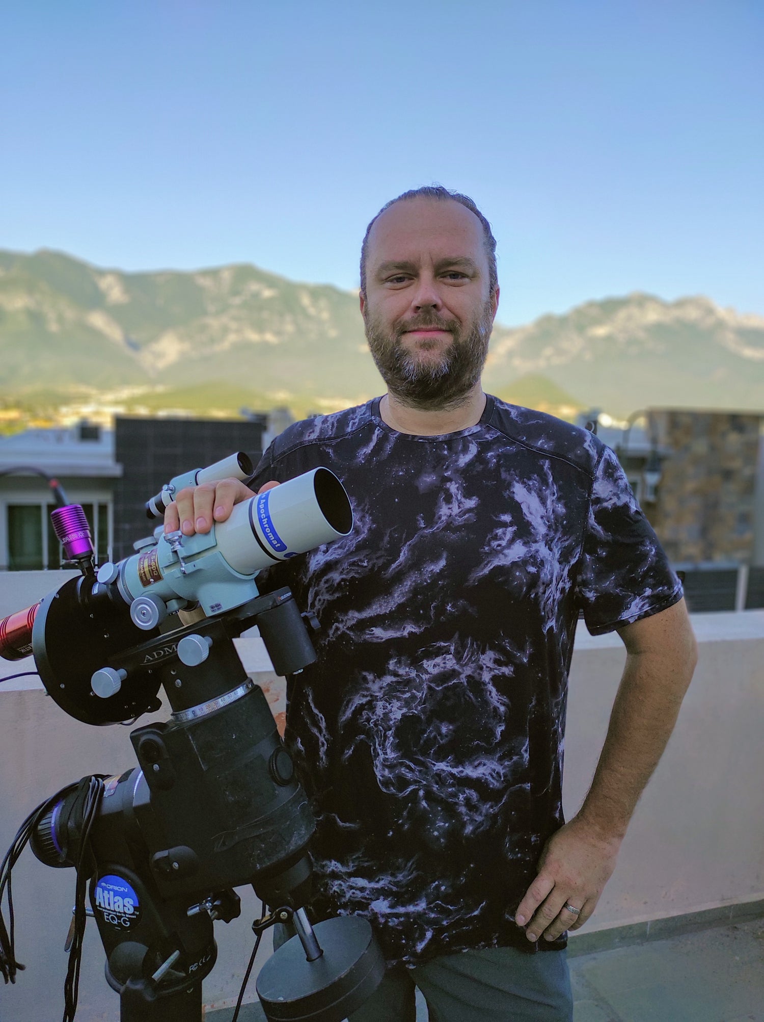 Pavel Vorobiev is holding a telescope on a rooftop with mountains in the background
